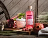 En flaska Koskenkorva Rhubarb står bredvid en drink, granatäpplen och rabarber.