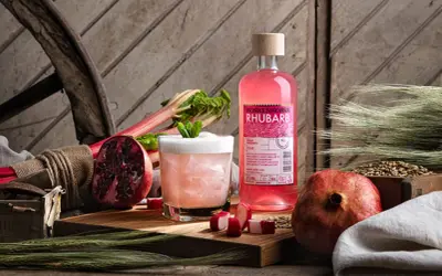En flaska Koskenkorva Rhubarb står bredvid en drink, granatäpplen och rabarber.