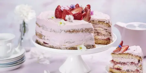 En vacker jordgubbstårta med rosa frosting och färska jordgubbar. En bit är uppskuren och ligger på en separat tallrik.