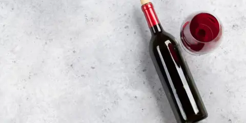 En flaska tamaral vin och ett glas rött vin på ett grått, stenig bakgrund.