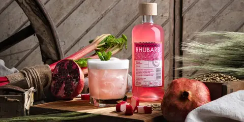 En flaska Koskenkorva Rhubarb står bredvid en drink, granatäpplen och rabarber.