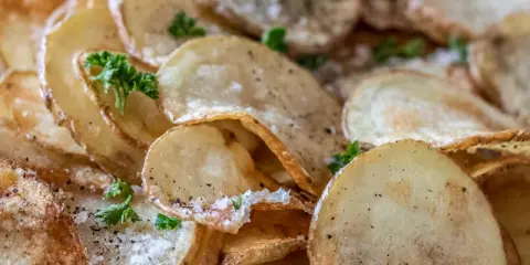 Krispiga, gyllene skivor av friterad potatis, strödda med salt och peppar, toppade med färsk persilja.