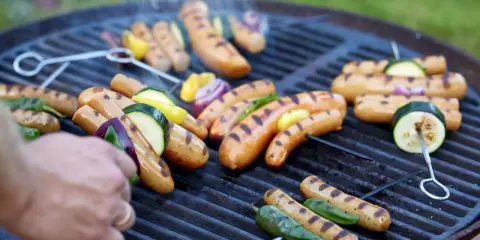 Grillad korv med grönsaker på en het grill. Röken stiger och doften sprider sig.