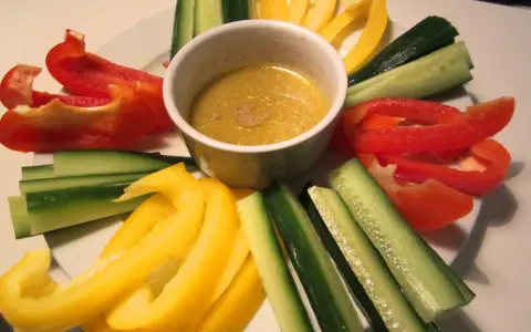 En skål med bagna cauda-sås omgiven av färgglada grönsaksstavar: röd och gul paprika samt gurka.