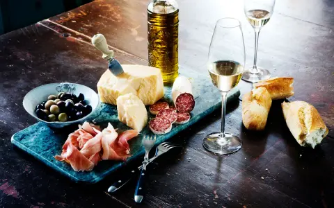 En härlig italiensk buffé med ost, salami, prosciutto, oliver, bröd och ett glas vitt vin, kanske en riesling druva.