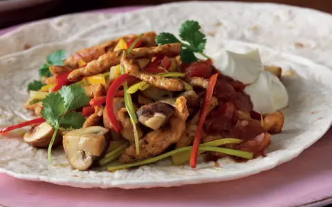 En läcker portion fajitas kyckling med paprika, champinjoner och gräddfil på en tortilla.
