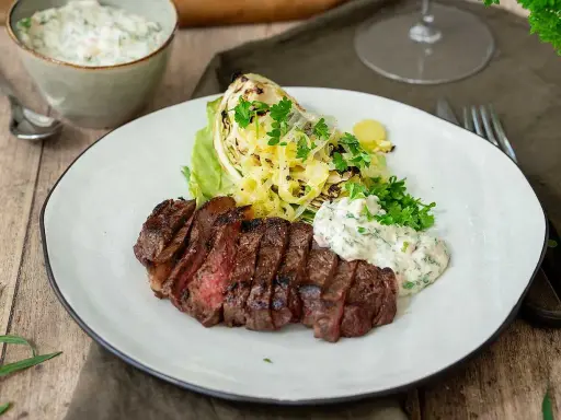En saftig grillad ryggbiff serveras med krispig sallad, grillad kål och en krämig sås.