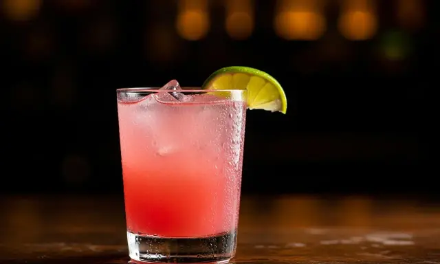 En rosa tequila drink med is och en limeklyfta på en mörk bakgrund.