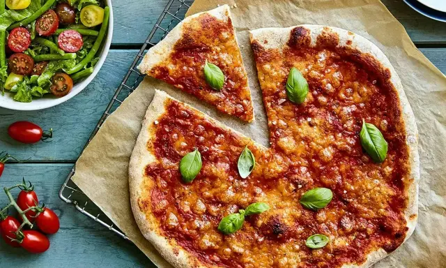 En härlig hemmagjord pizza med tomatsås och ost, toppad med färsk basilika. Bredvid en fräsch sallad med gröna bönor och körsbärstomater.