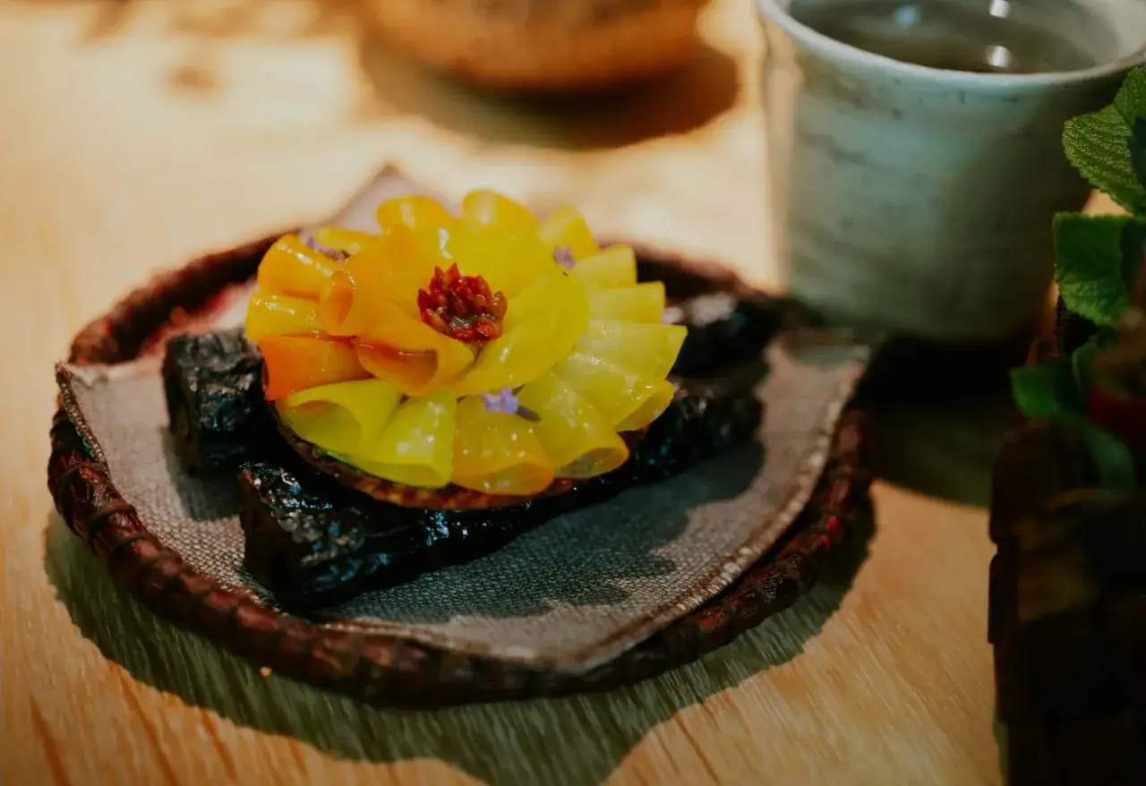 En konstn&auml;rlig dessert med gula och orangea blad, som en blomma, serverad p&aring; en m&ouml;rk bas. En upplevelse fr&aring;n en michelin restaurang sverige.