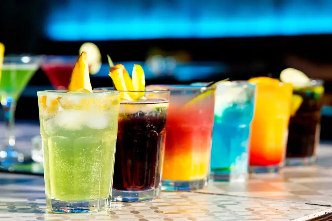 En rad f&auml;rgglada drinkar, inklusive en uppfriskande tequila drink med lime och is, st&aring;r redo att avnjutas.