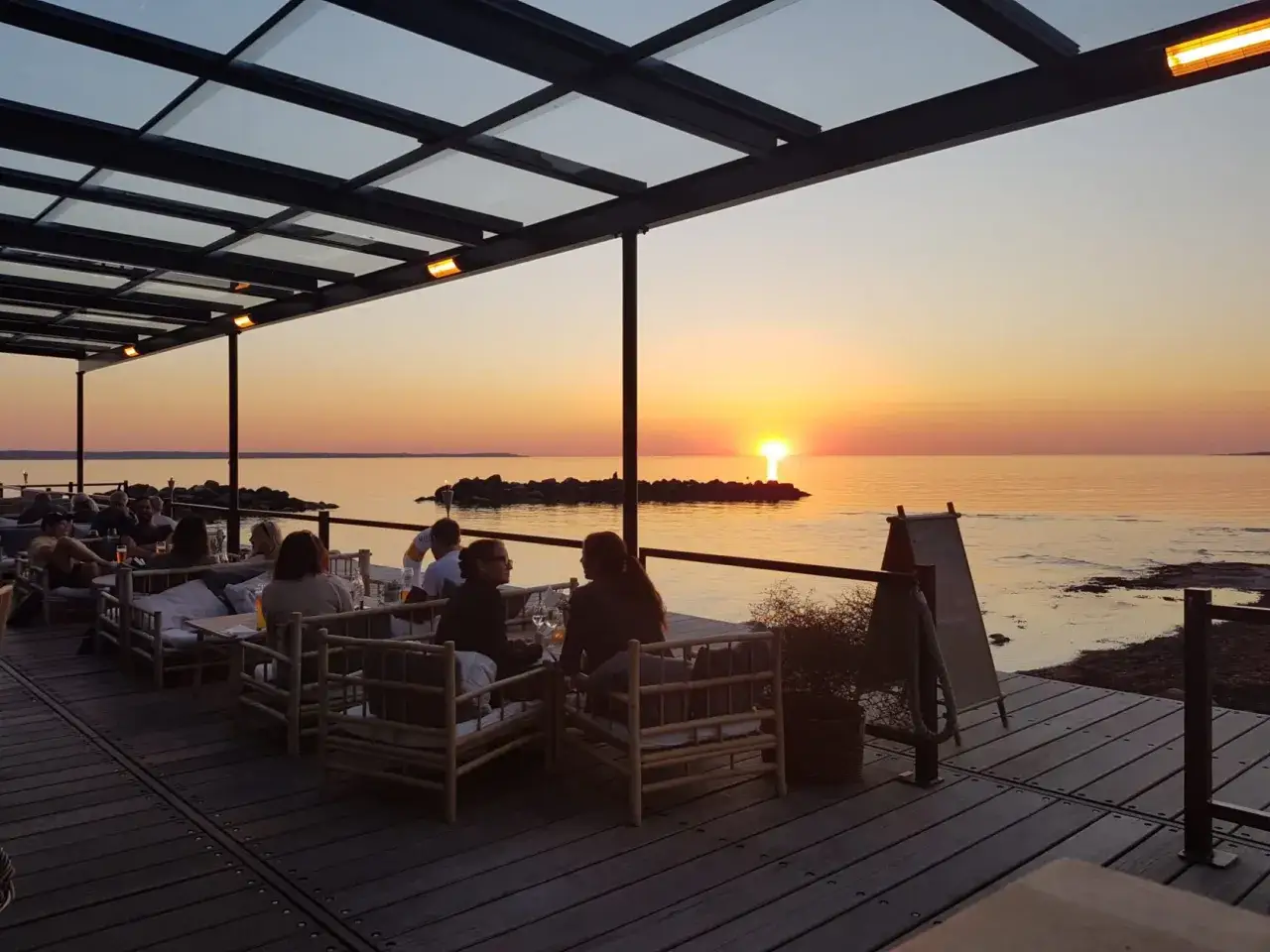 En restaurang vid havet med g&auml;ster som njuter av solnedg&aring;ngen.