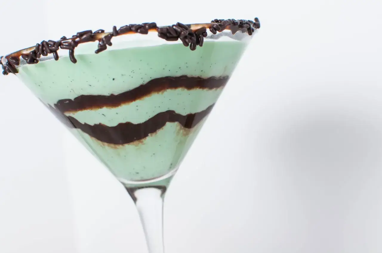 Grön, krämig Grasshopper drink med chokladströssel på kanten och chokladsås virvlad inuti.