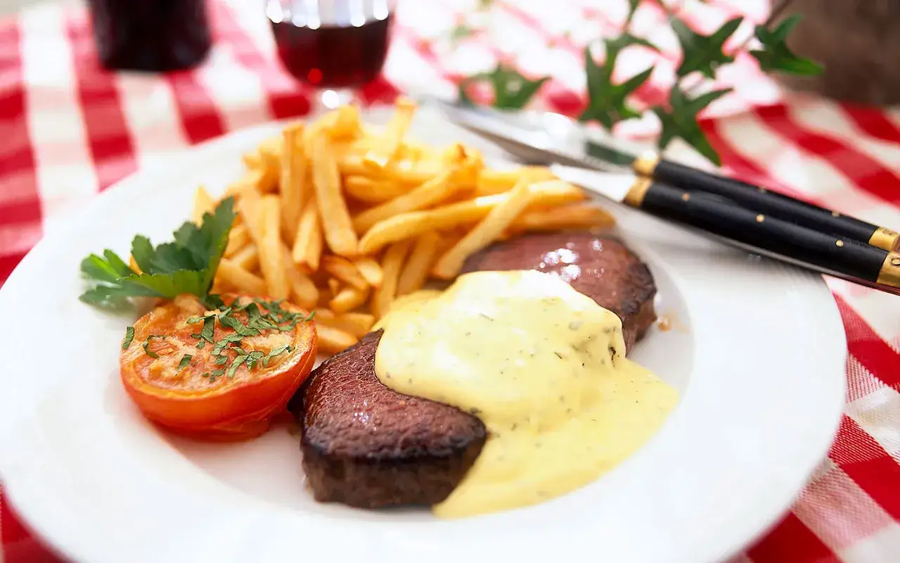 En klassisk steak frites med pommes frites, en halverad tomat och en kr&auml;mig s&aring;s.