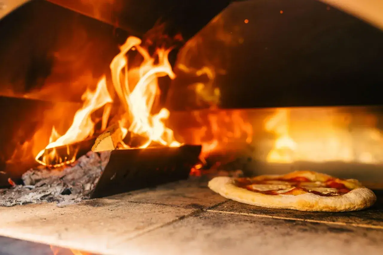 En vedugnsbakad pizza med ost och tomats&aring;s gr&auml;ddas i en varm ugn med flammande eld.