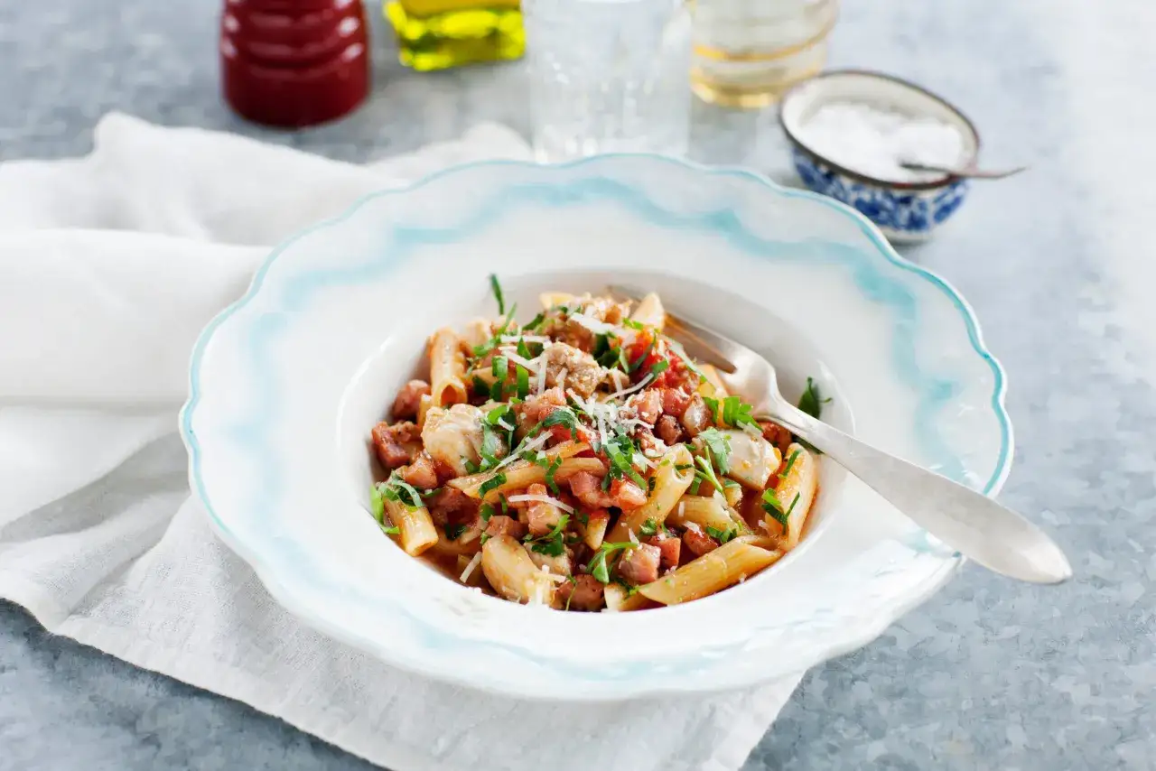 En tallrik med penne pasta, kyckling och tärnad pancetta, toppad med persilja och parmesan. Ett enkelt pancetta recept för en god middag.