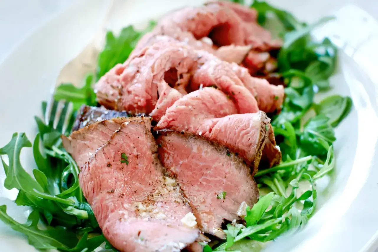 Skivor av saftig rostbiff, perfekt marinerad, serveras p&aring; en b&auml;dd av fr&auml;scha gr&ouml;na blad.