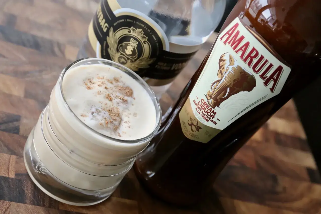 En kr&auml;mig Amarula drink, toppad med kanel, bredvid flaskan.